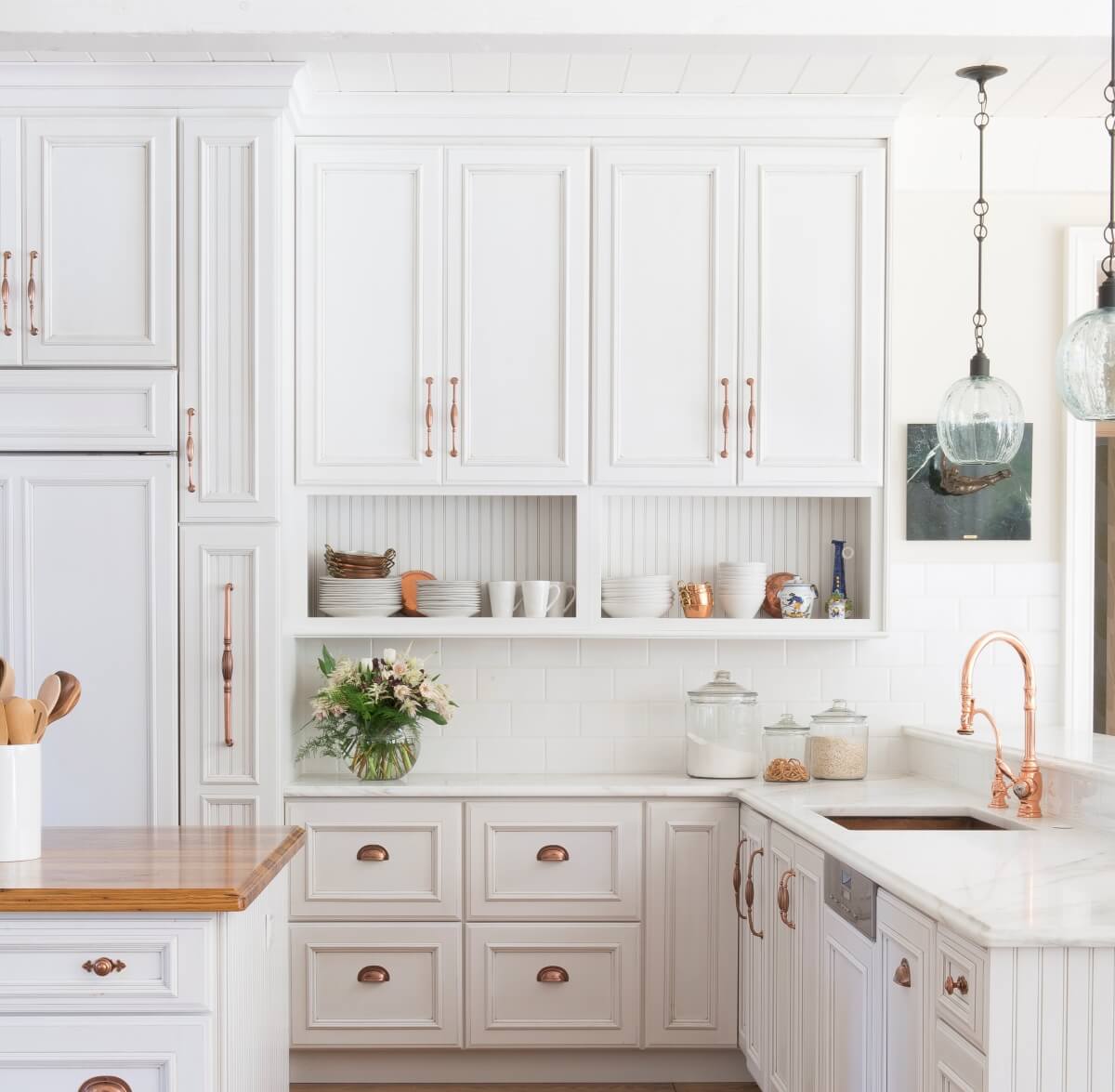 A French Farmhouse style kitchen remodel with bright white painted cabinets and copper hardware. A Dura Supreme kitchen featuring Wall Cabinets with Open Display Below.