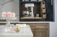A counter-sitting cabinet opens up to show a larger mixer on a flat roll-out shelf with apothecary storage to the side for misc. storage for baking tools & supplies.