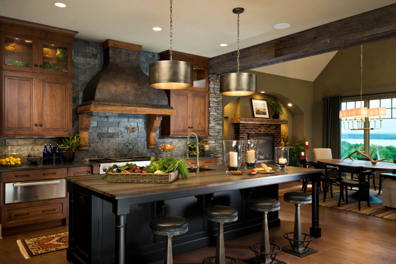 A Rustic Traditional styled kitchen design with a grand wood and metal hood, dark painted kitchen island, and distressed wood cabinets.