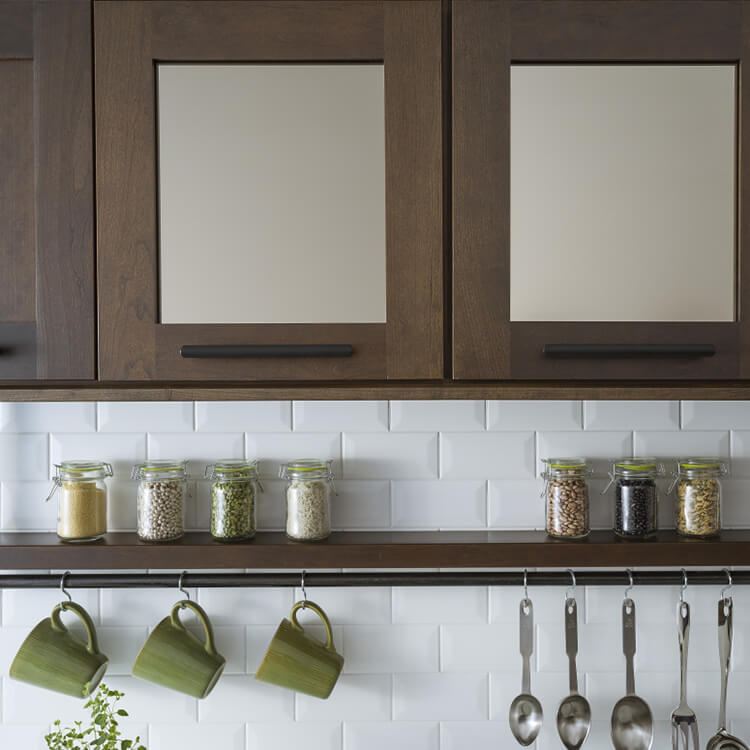 A close up image of mirror cabinet doors in with an industrial floating shelf in a modern kitchen design featuring Dura Supreme Cabinetry.