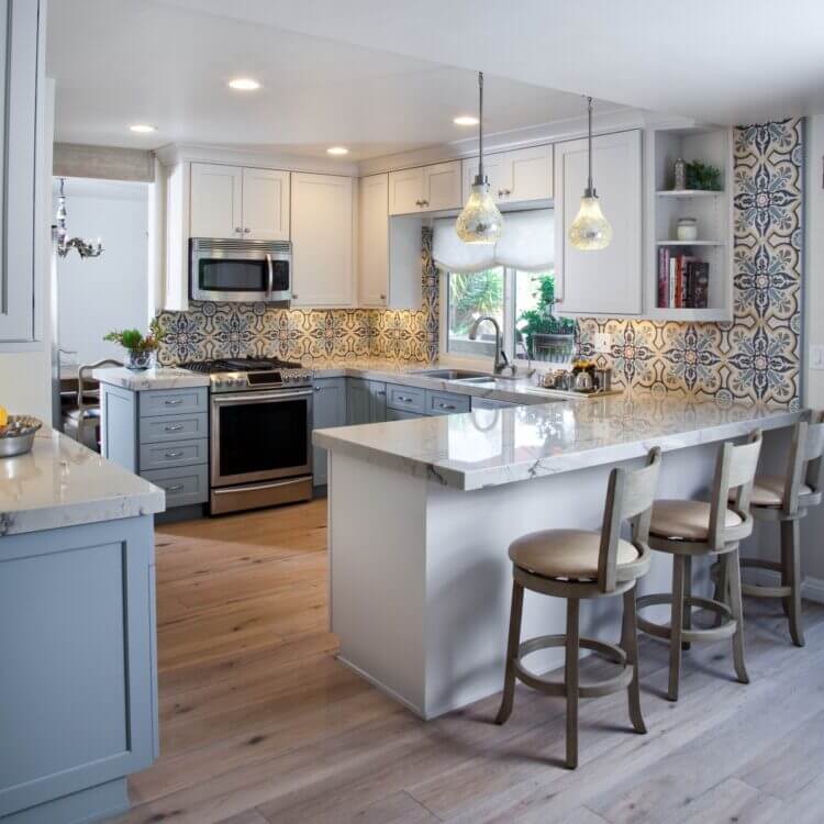A colorful kitchen with white and gray cabinetry and a colorful hand-painted tile backsplash.