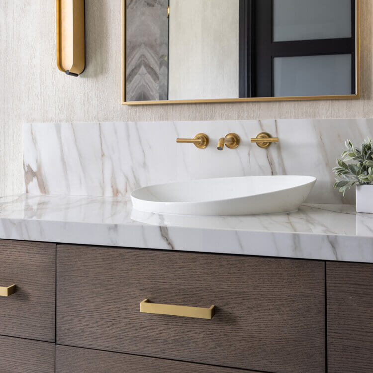 Dark true-brown stained custom bathroom vanity cabinets showcase a distinctive horizontal grain pattern for a modern, furniture-inspired look. Warm brass cabinet pulls complement the rich wood texture, while marble finishes add timeless elegance.