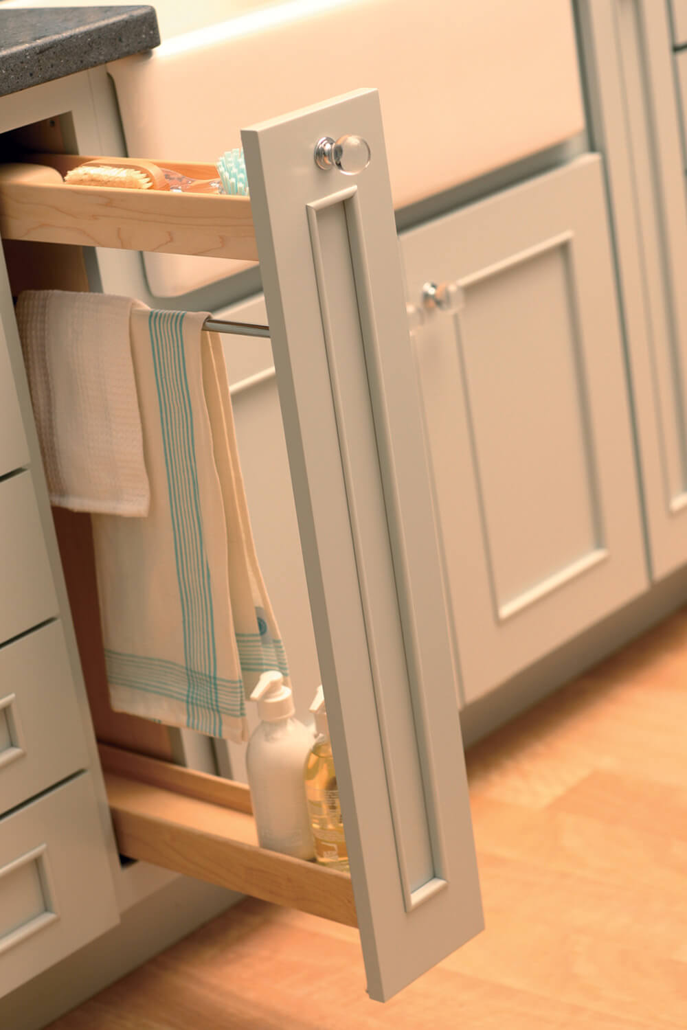 A Pull-Out Towel Bar cabinet by Dura Supreme provides a dedicated space for storing towels, sponges, soaps, and hand-sanitizers next near the sink area.