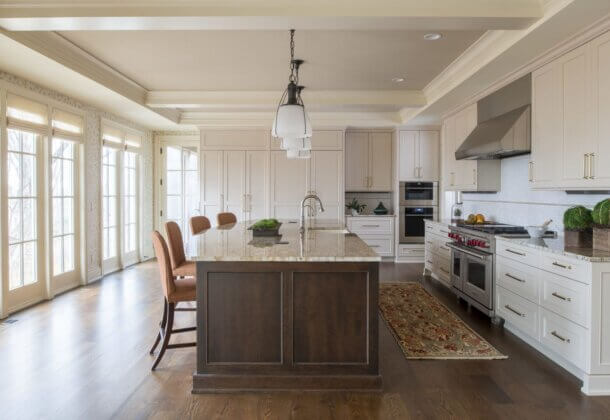 A classic traditional styled kitchen design with a dark stained kitchen island with countertop seating and white painted cabinets. A wall of windows brings in lots of natural light.