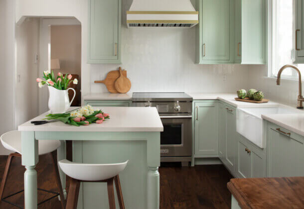 A colorful kitchen with minty green painted cabinets and a white range hood with gold hardware and accents.