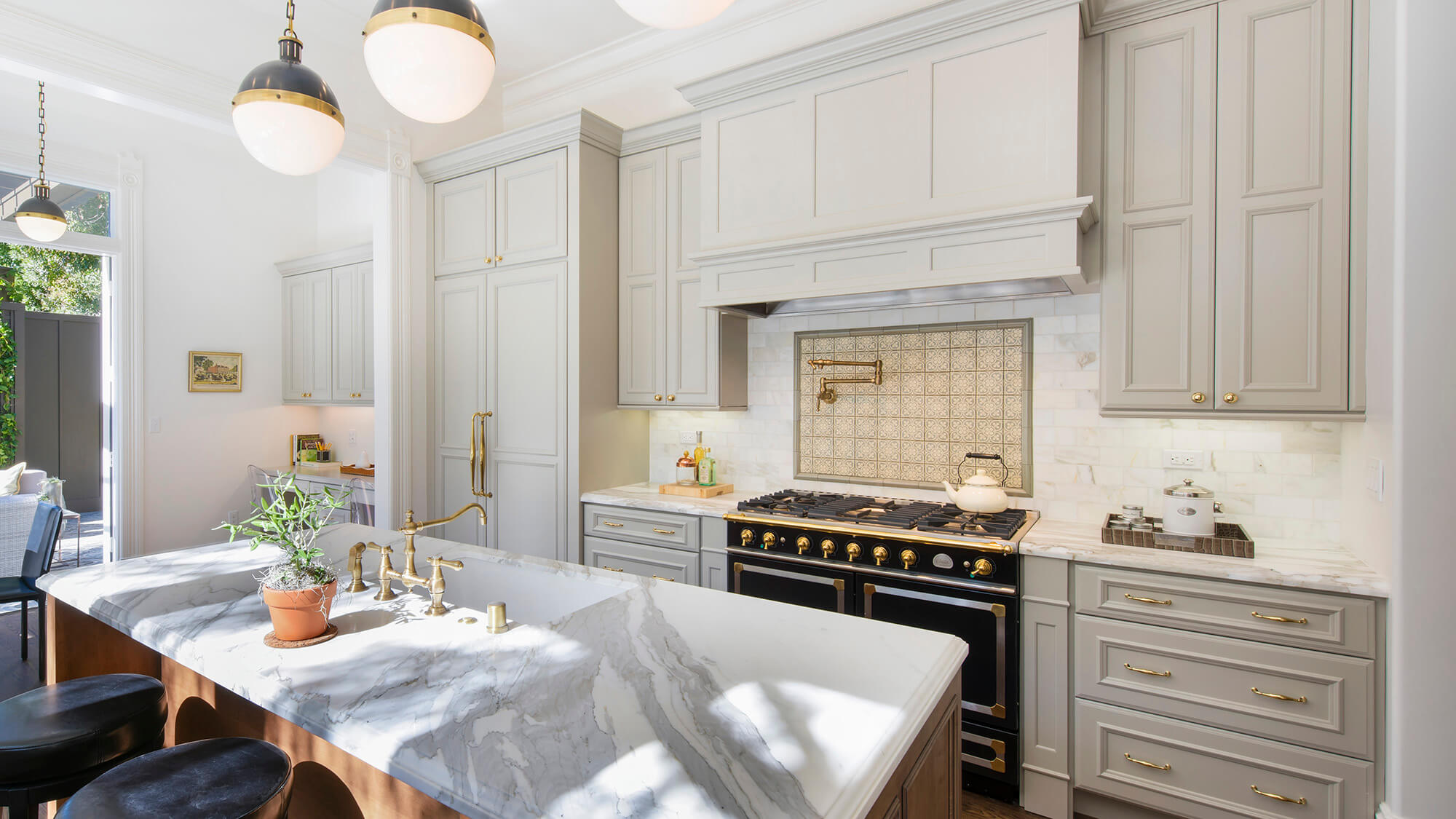 Beautiful slide-in, black and gold range with double ovens showing gray painted cabinets paired with brass cabinet hardware and fixtures. Featuring Dura Supreme kitchen cabinets and traditional styled wood hood canopy.