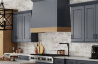 A close up of the two-toned wood hood and kitchen cabinets in a dark navy blue paint and light stained cherry wood.