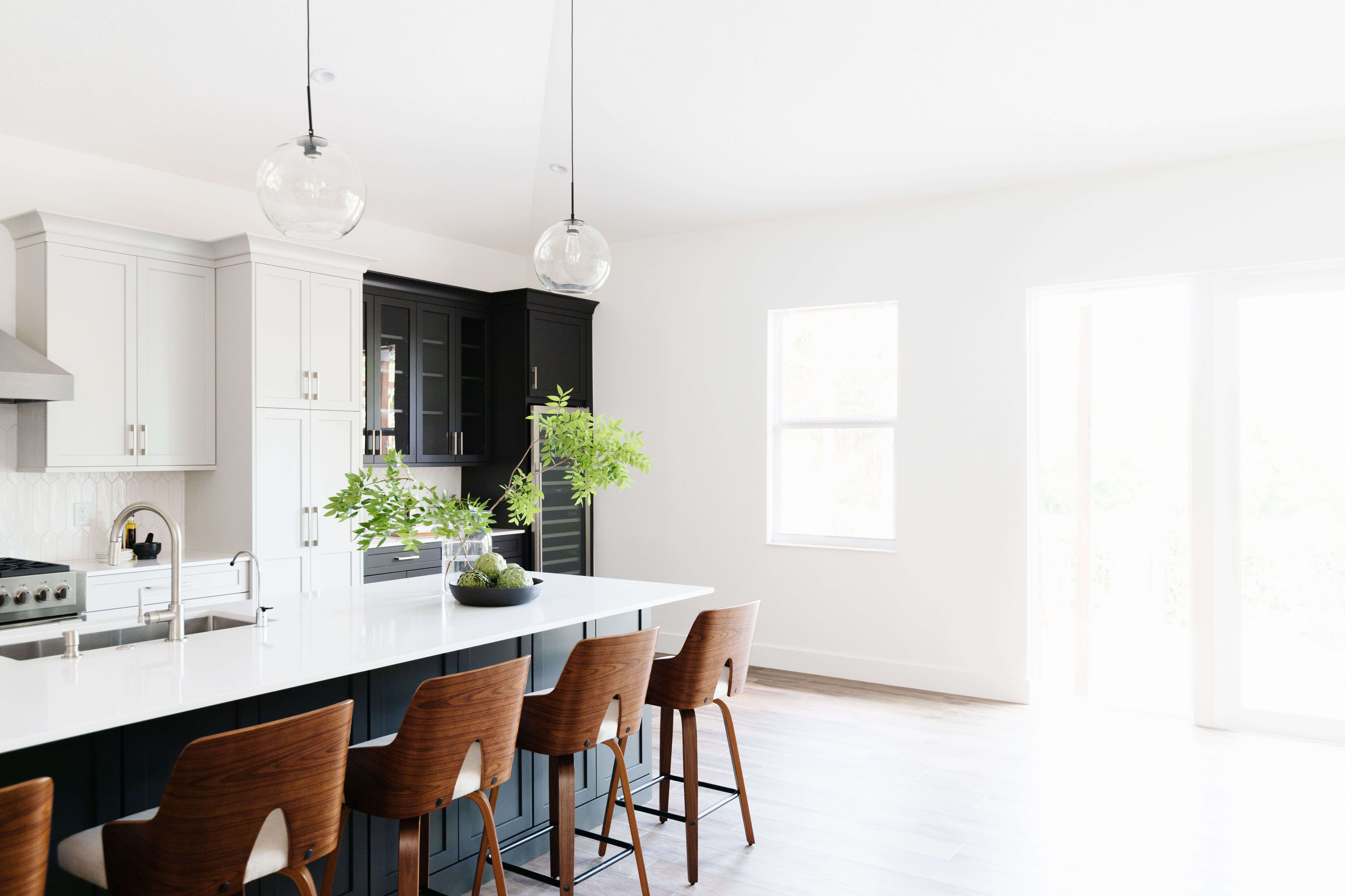 A black painted kitchen island with Mid-Century Modern style bar stools and bright white walls and kitchen cabinets.