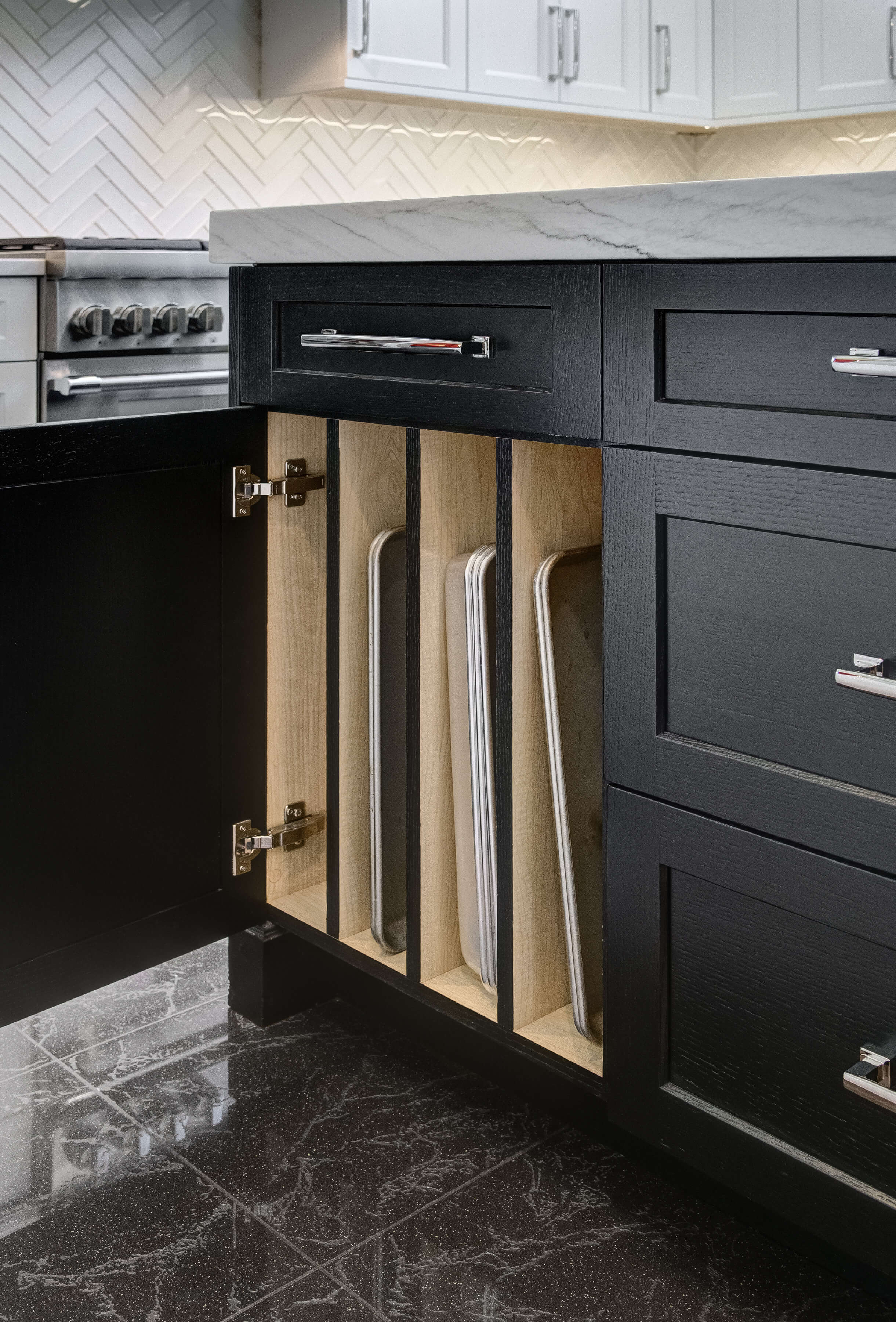 A kitchen island with black painted oak finish showing an open cabinet with organized storage for baking sheets.