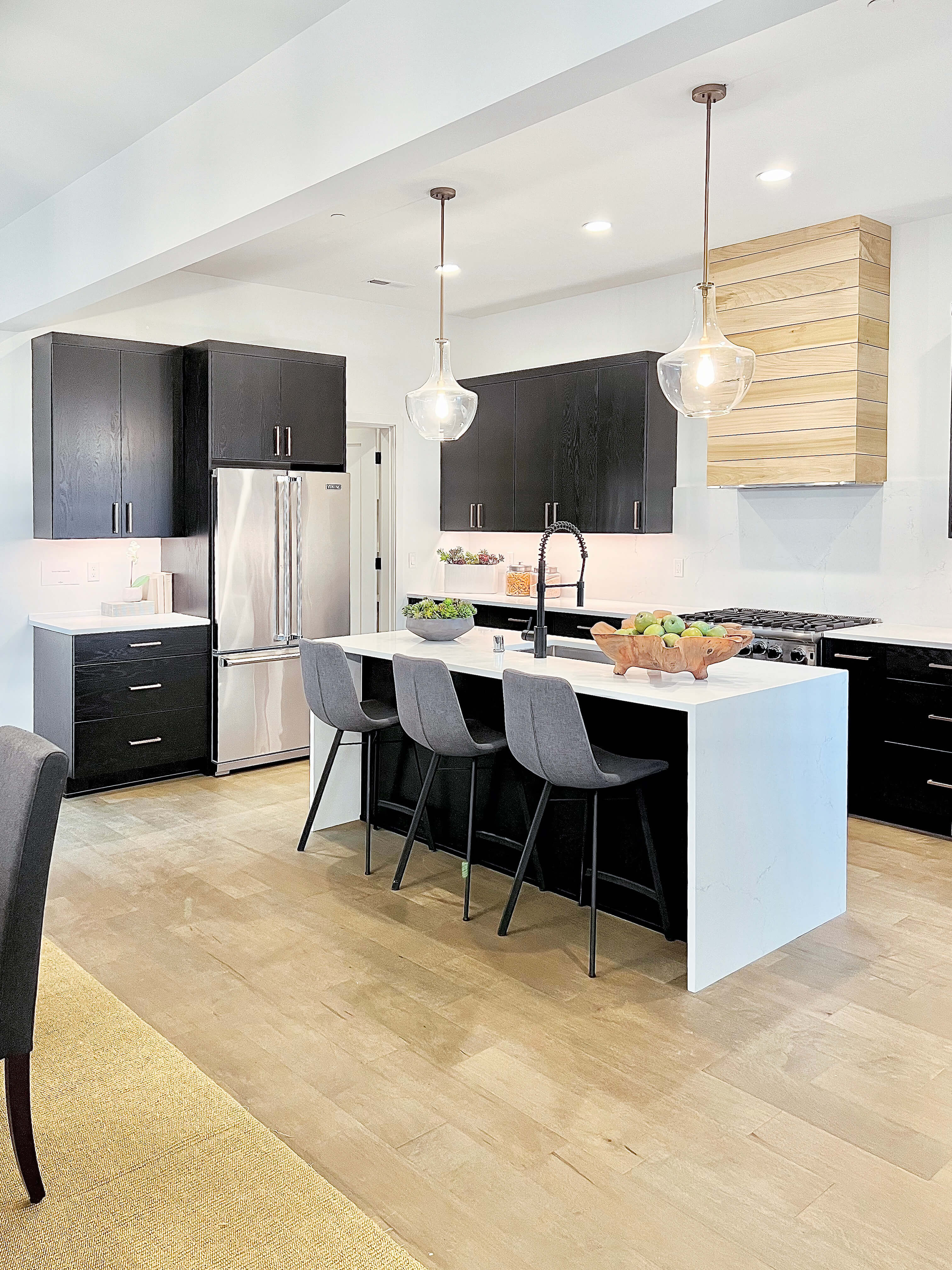A contemporary kitchen design with textured, black painted oak cabinets and a light stained wood hood with shiplap details all from Dura Supreme.
