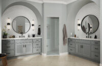 Double vanities in a large master bathroom with arched insets into the wall with gray paint and reeded cabinet doors.