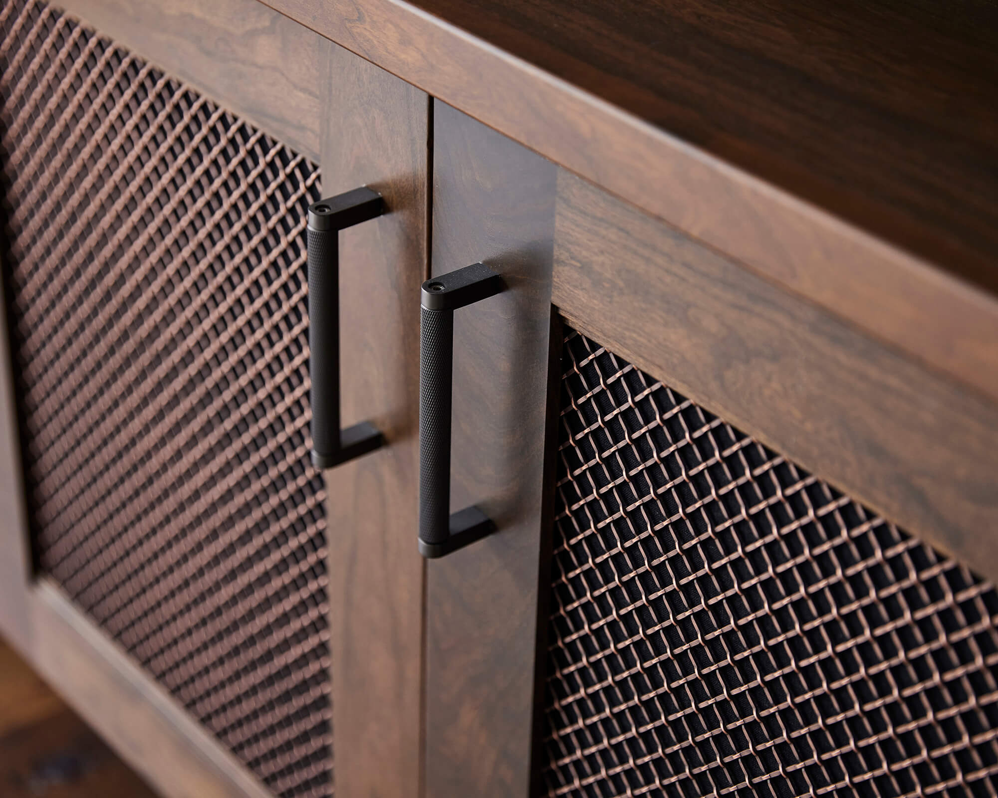 A close up of an industrial style cabinet with wire mesh inserts, black pulls, and dark brown stained wood.