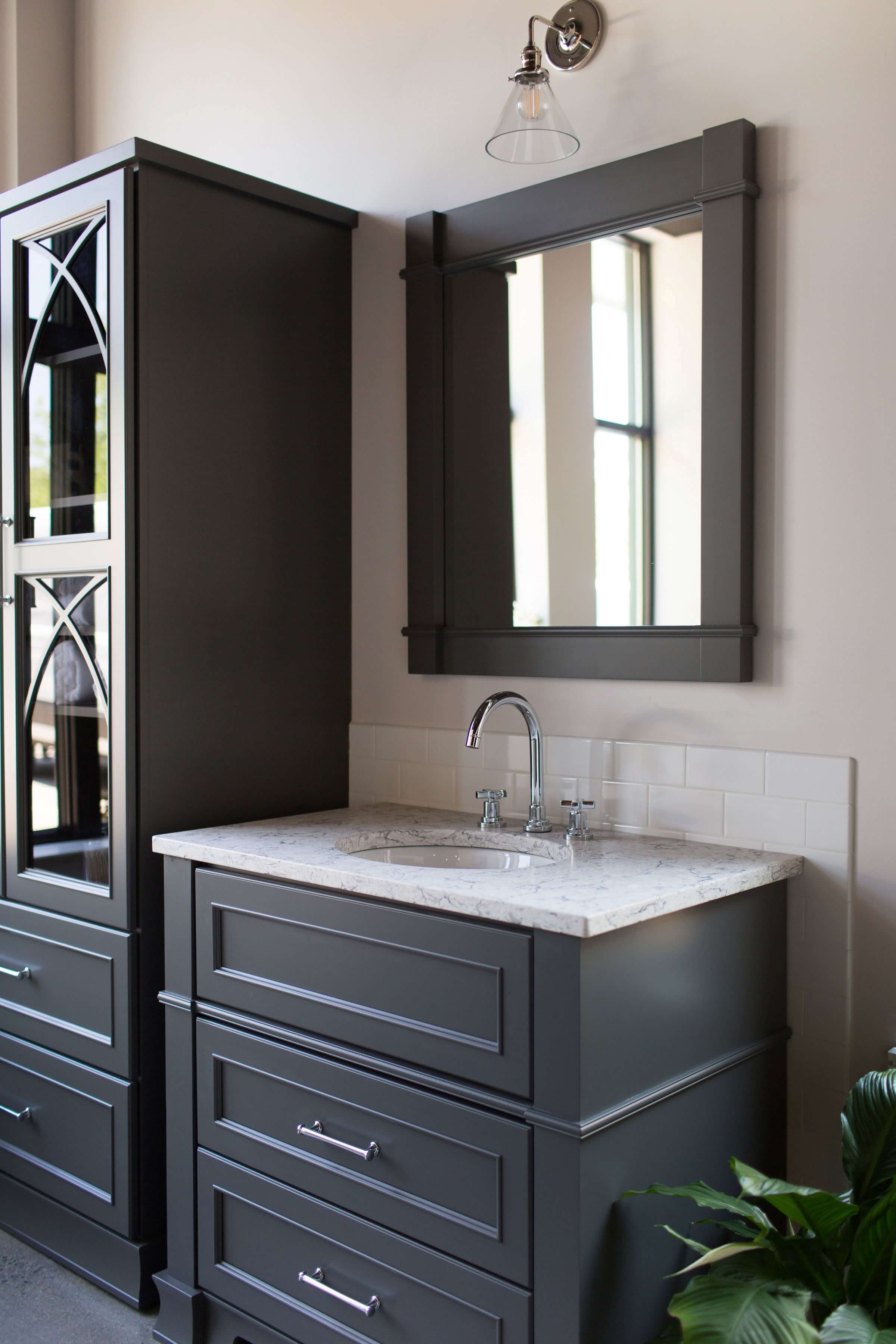 A dark gray painted collection of bathroom furniture from Dura Supreme featuring a free standing linen cabinet with a matching furniture style vanity.