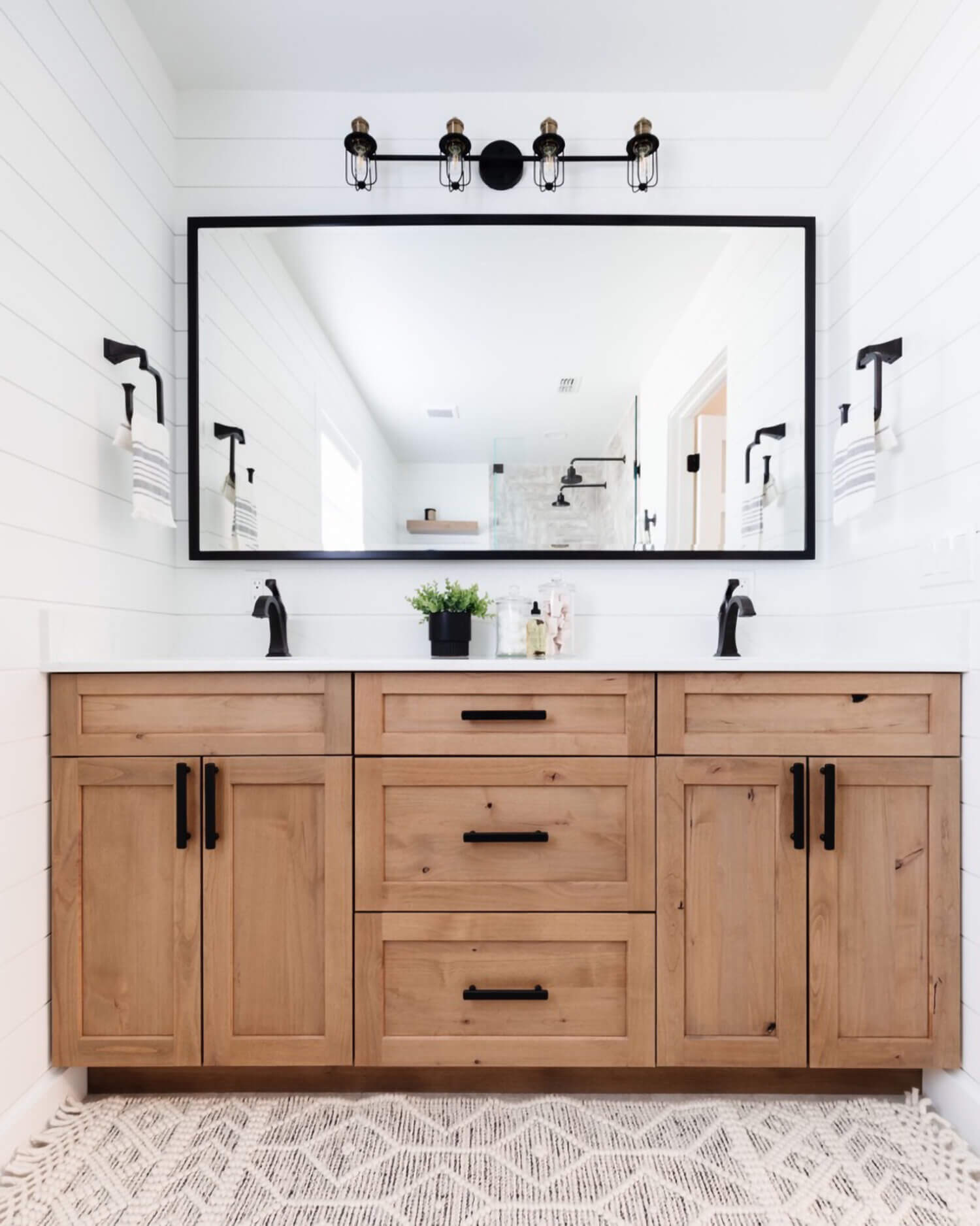 An elegant modern farmhouse bathroom with a rustic knotty alder vanity in a light stain with industrial style fixtures and hardware.