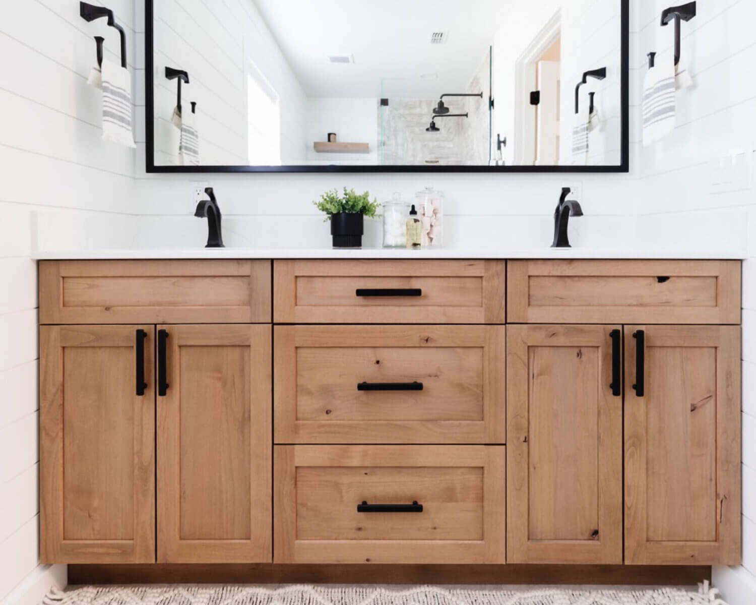 An elegant modern farmhouse bathroom with a rustic knotty alder vanity in a light stain with industrial style fixtures and hardware.