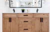 An elegant modern farmhouse bathroom with a rustic knotty alder vanity in a light stain with industrial style fixtures and hardware.