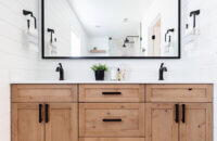 An elegant modern farmhouse bathroom with a rustic knotty alder vanity in a light stain with industrial style fixtures and hardware.