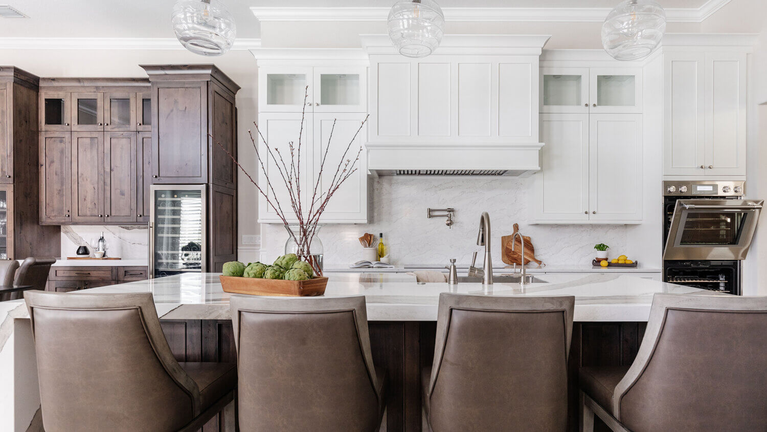 A transitional and casual kitchen design with elegant finishes. A grand white painted wood hood takes center stage over the knotty alder kitchen island.