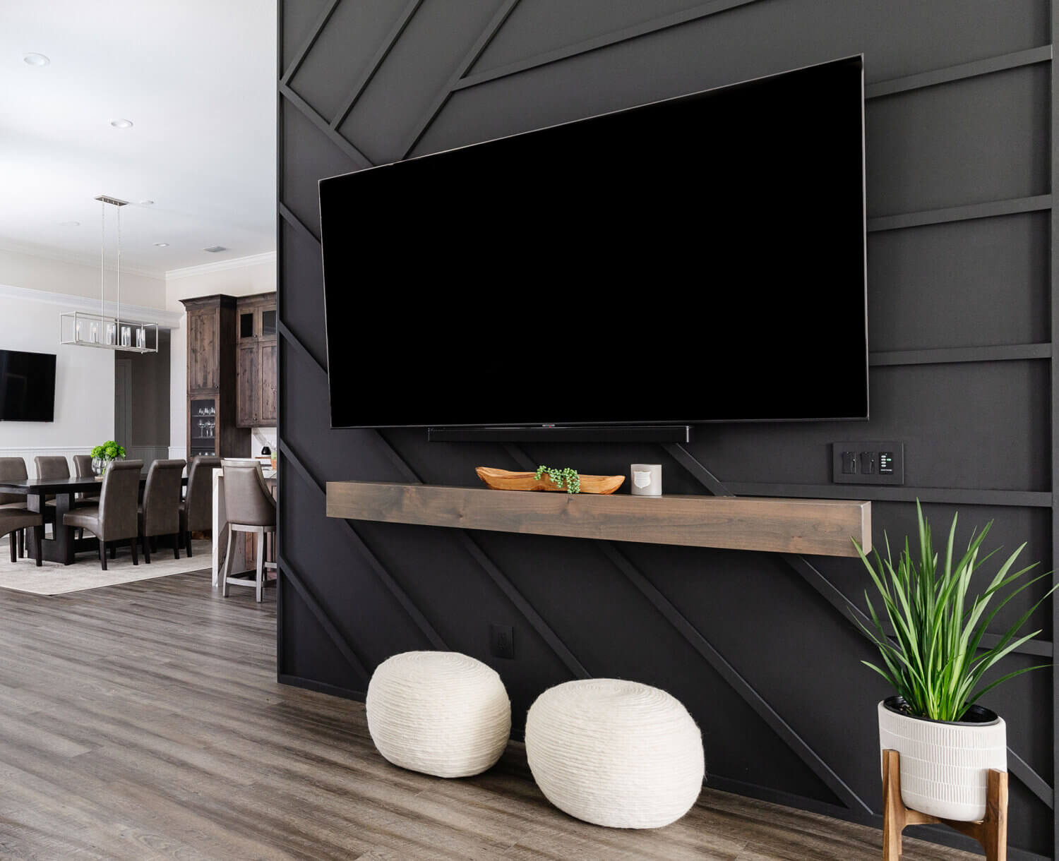 The TV wall with a suspended TV on a black paneled wall with a unique pattern and floating mantel shelf below the TV.