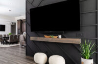 The TV wall with a suspended TV on a black paneled wall with a unique pattern and floating mantel shelf below the TV.