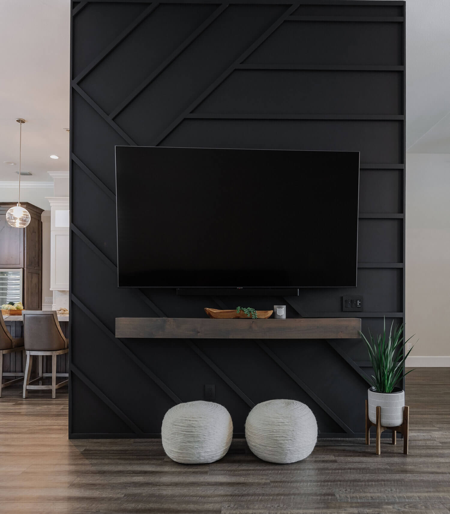 The TV wall room divider with a suspended TV on a black paneled wall with a unique pattern and floating mantel shelf below the TV.