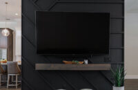 The TV wall room divider with a suspended TV on a black paneled wall with a unique pattern and floating mantel shelf below the TV.