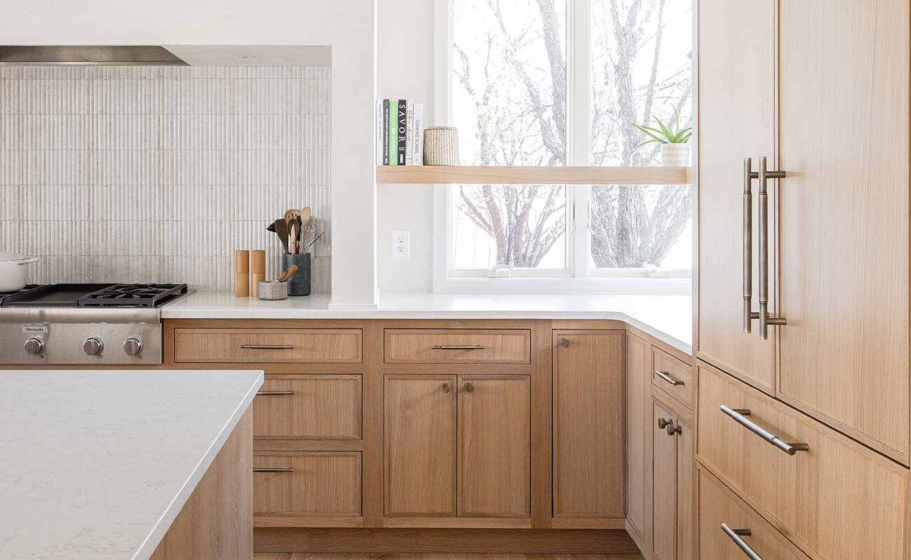 A stunning quarter-sawn white oak kitchen with light-stained skinny shaker cabinets and a white range alcove with a floating shelf in a corner kitchen window.