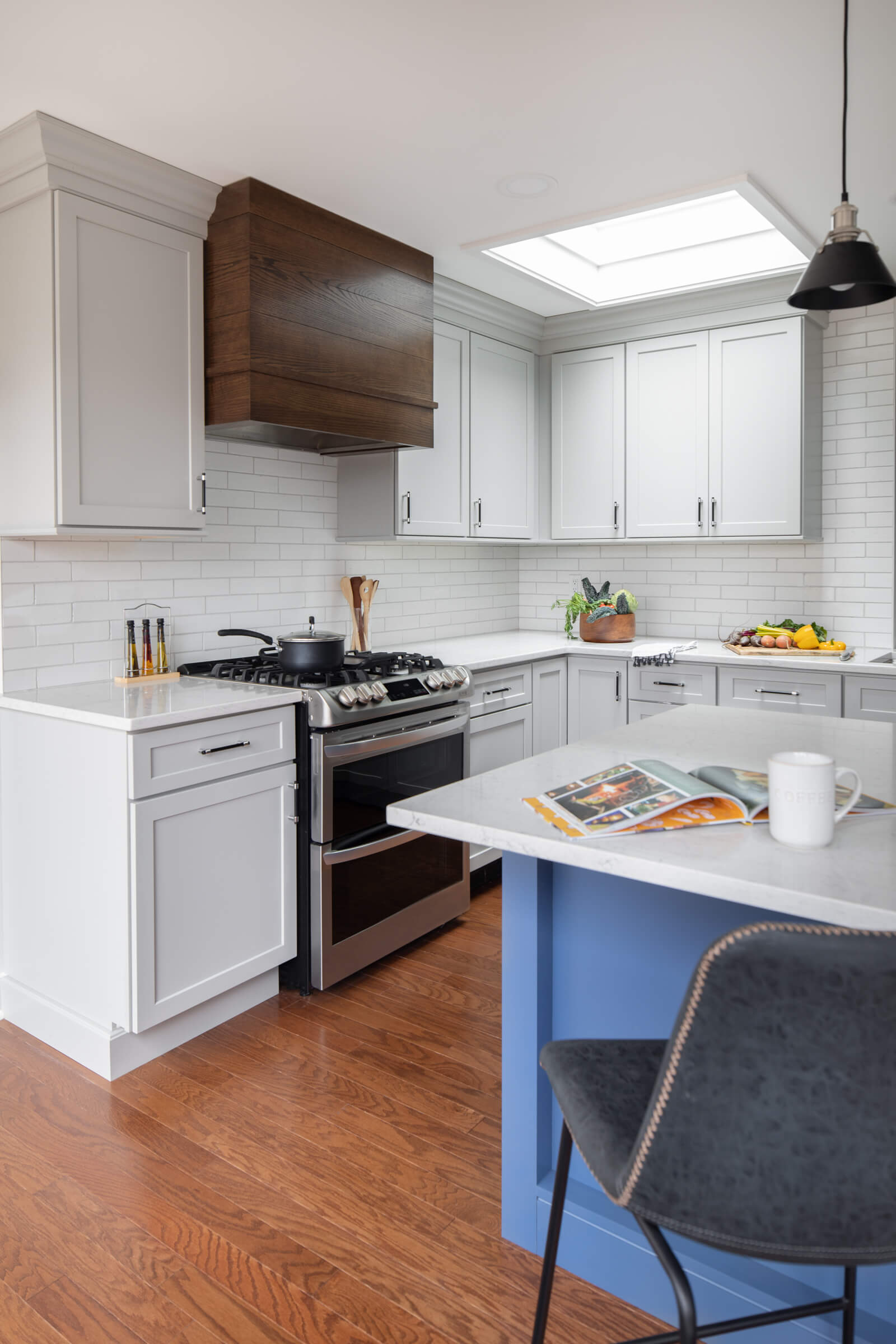 A three-toned kitchen featuring a Red Oak wood hood paired with a white paint for the perimeter cabinets and a light blue paint for the kitchen island.