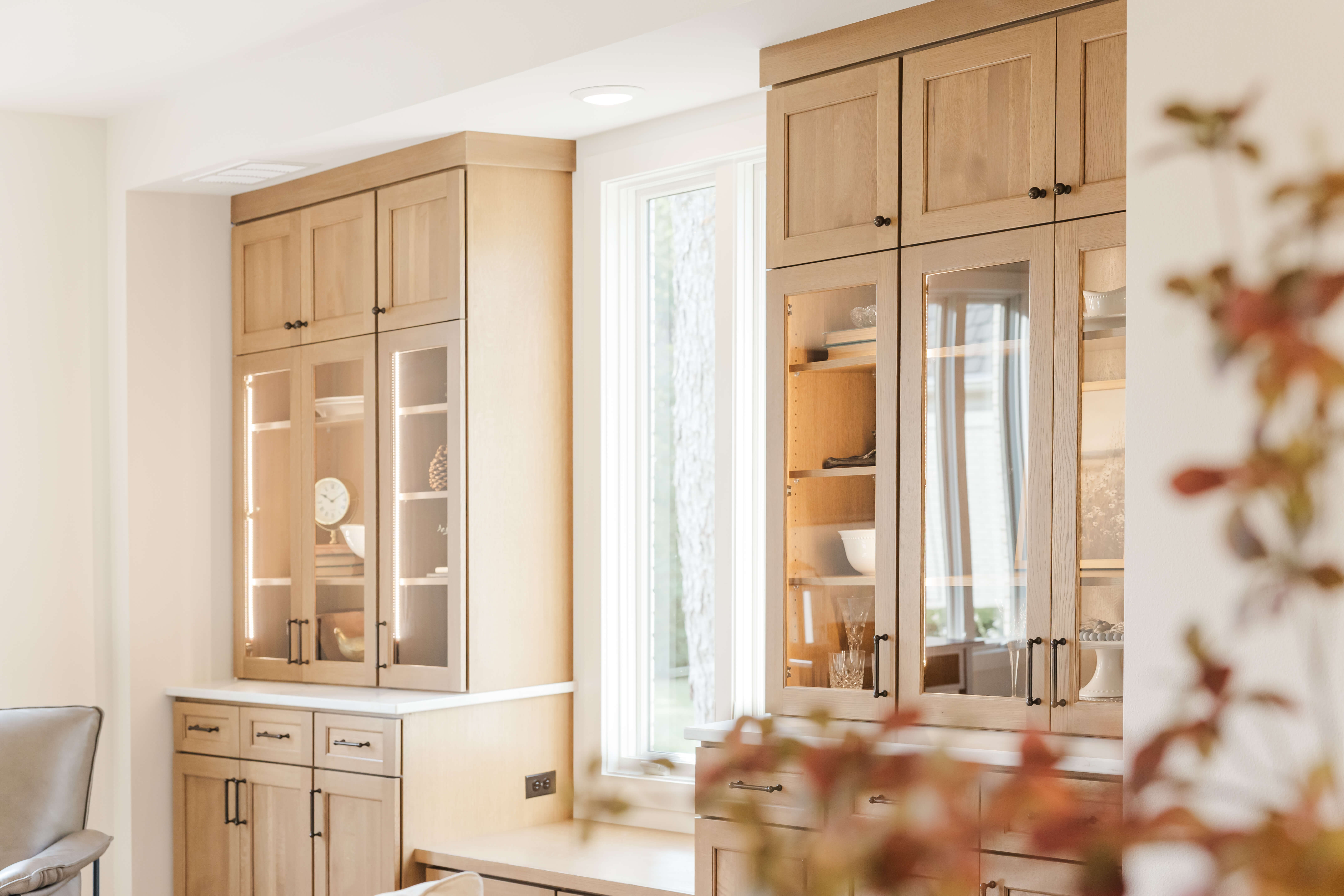 Built in cabinets in a light stained wood finish surround the dining room window, creating a beautiful focal point with abundant storage and display space. A built-in boot bench, glass-front cabinets, and warm brass cabinet hardware combine function and timeless style.