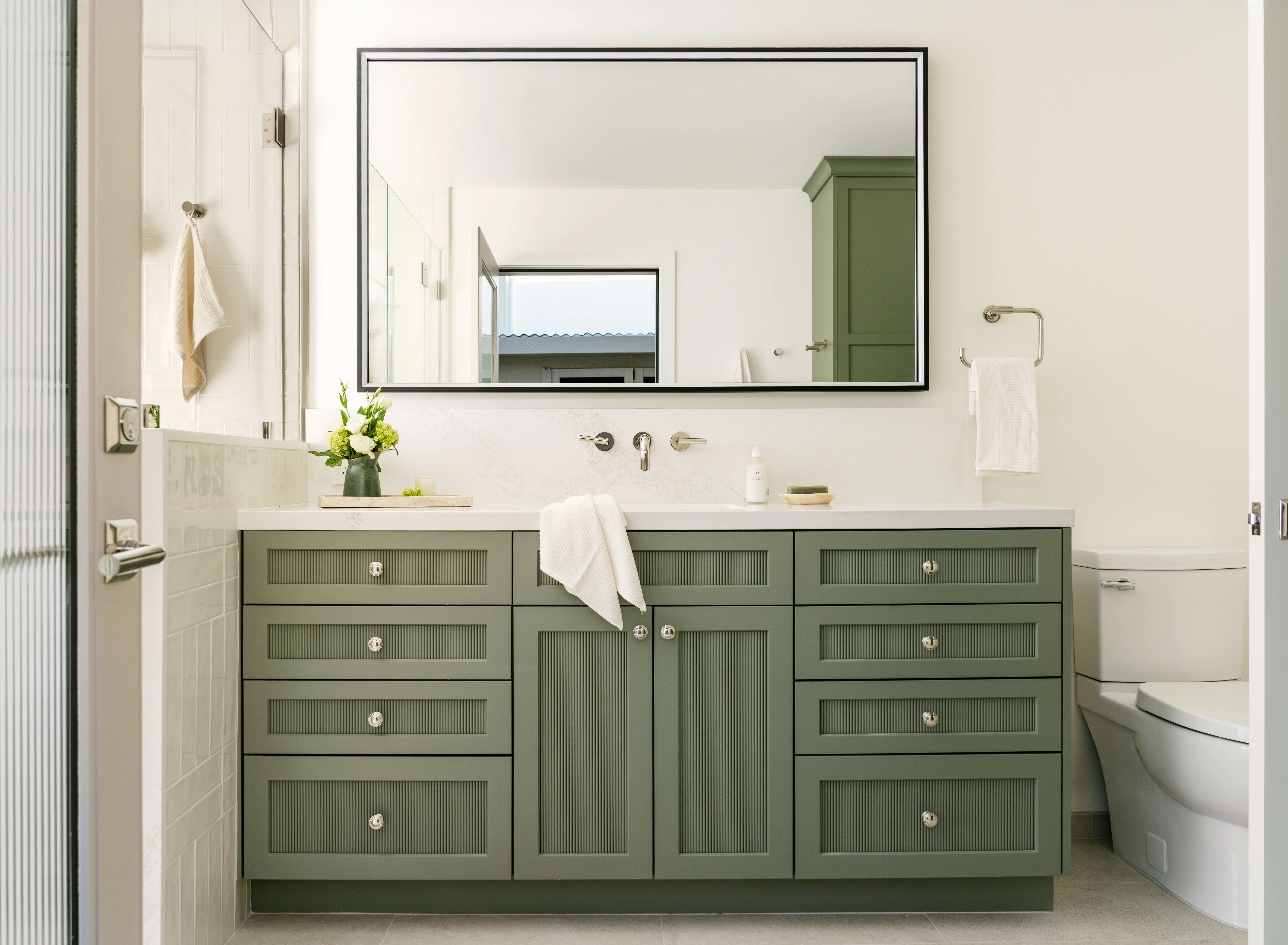 Custom bathroom vanity in a trendy light green painted finish features reeded cabinet door panels and drawers accented with polished round cabinet knobs. This furniture-inspired design adds texture, storage, and character while creating a fresh, sophisticated bathroom aesthetic.