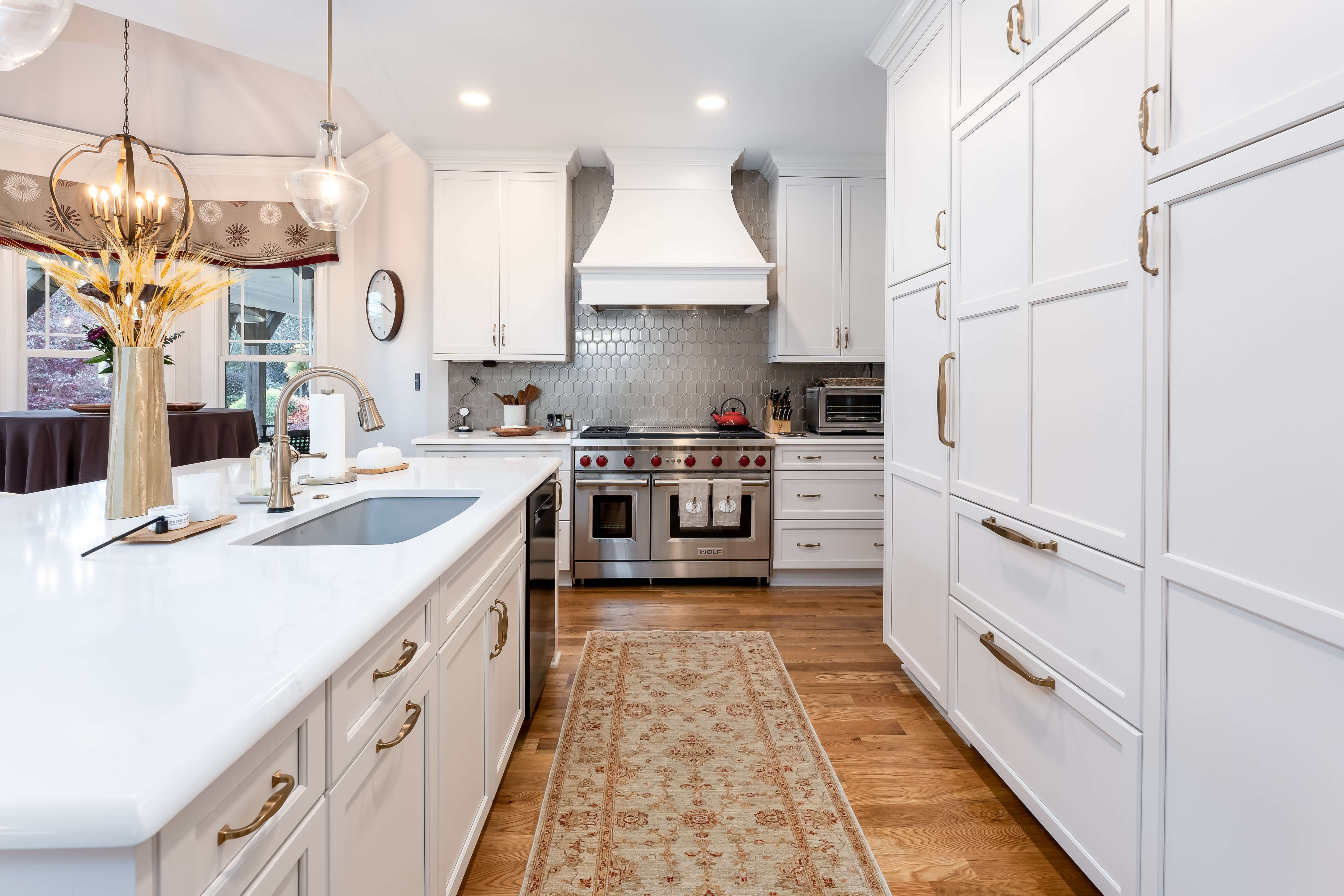 Classic white painted custom kitchen cabinets create a timeless, elegant design with detailed door styling and traditional cabinet hardware. Warm brass-toned pulls and knobs complement the bright cabinetry, while a large kitchen island anchors the welcoming gathering space.