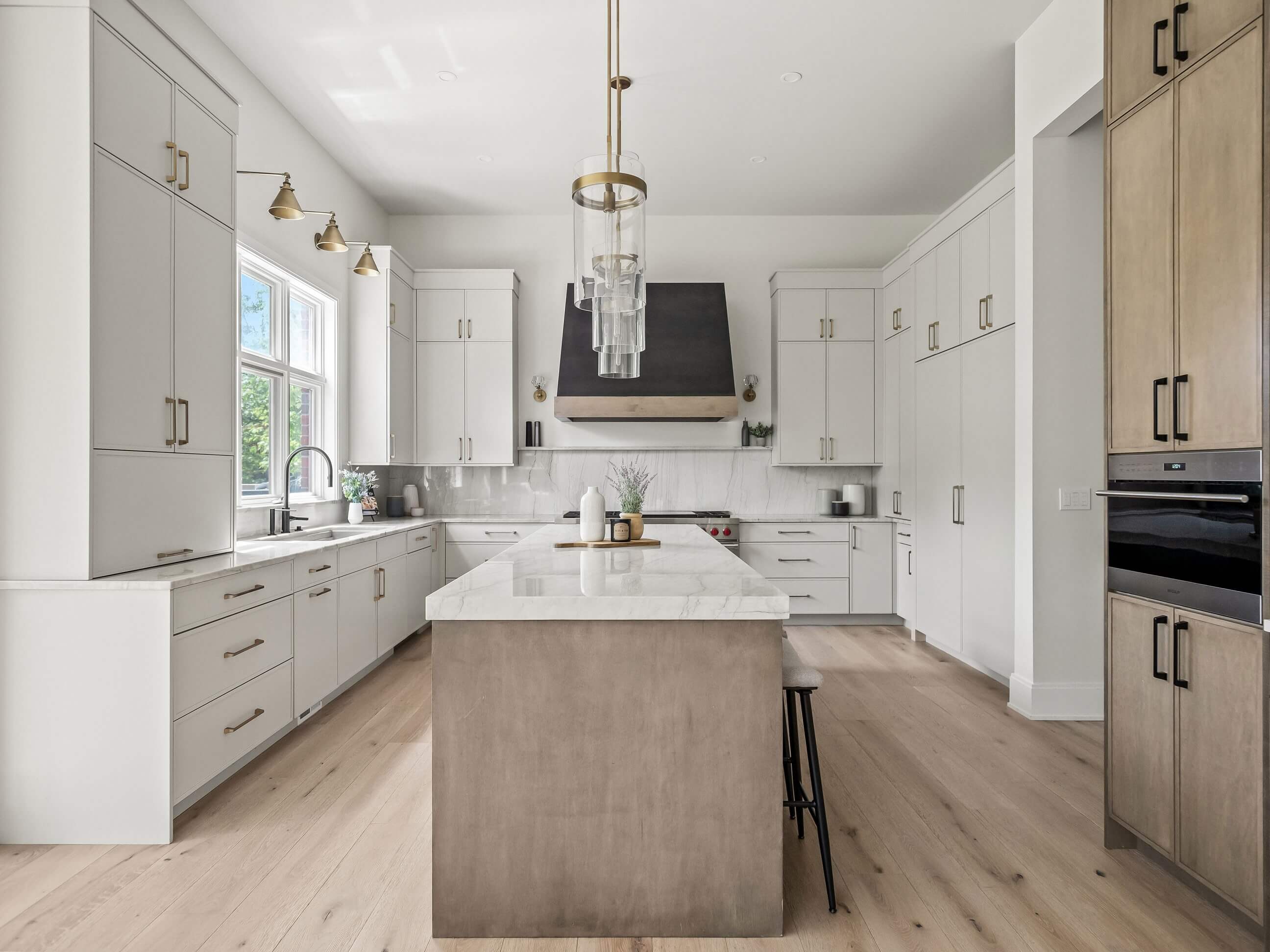 Three-tone custom kitchen cabinets feature white painted perimeter cabinetry, a dark charcoal island, and warm wood accents with trendy skinny shaker cabinet doors. Modern black cabinet hardware adds bold contrast, creating a clean, contemporary kitchen design.
