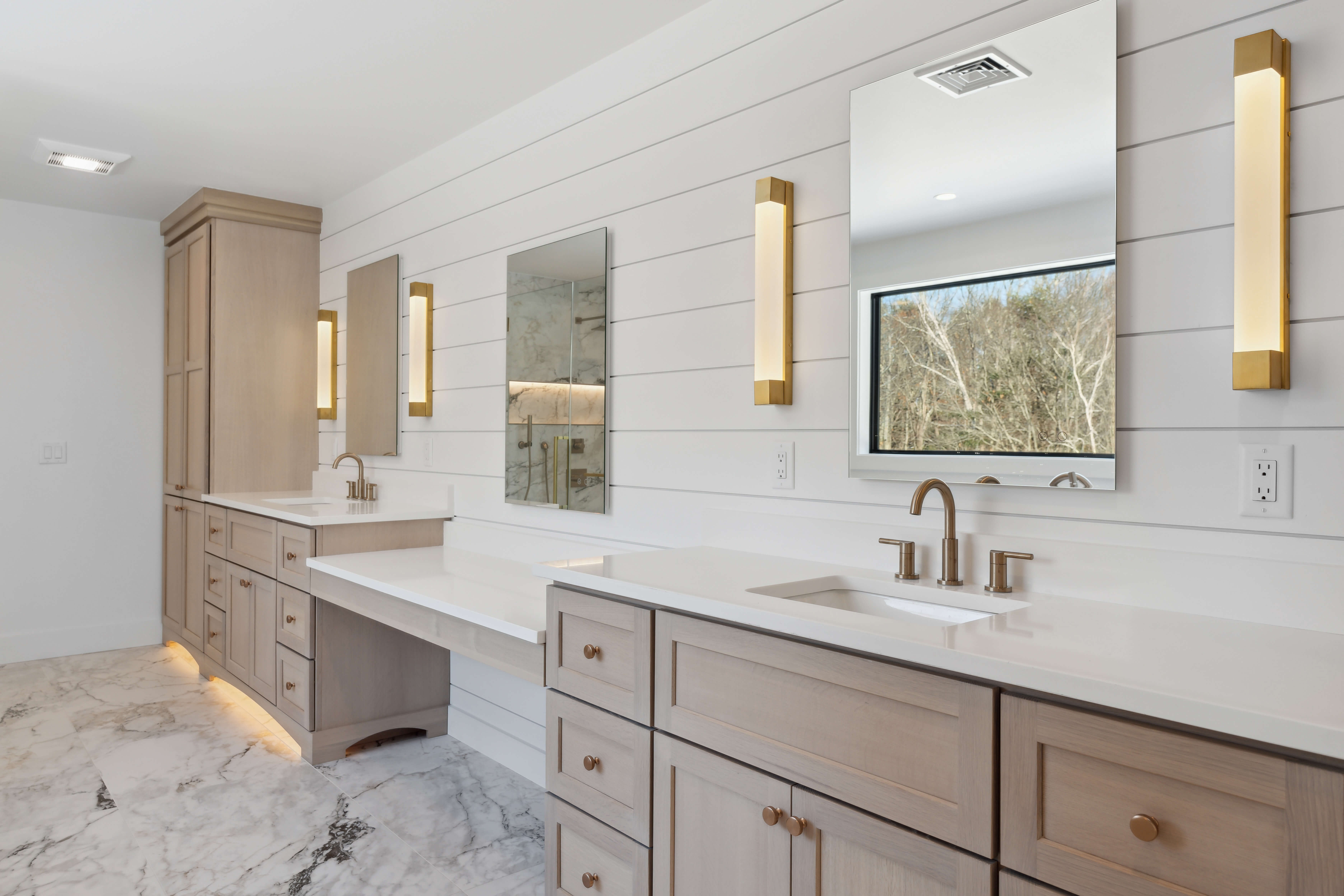 Light stained wood custom bathroom vanity cabinets pair beautifully with elegant gold cabinet hardware for a warm, sophisticated look. Extensive drawer storage, clean lines, and bright finishes create a luxurious and highly functional bathroom design.