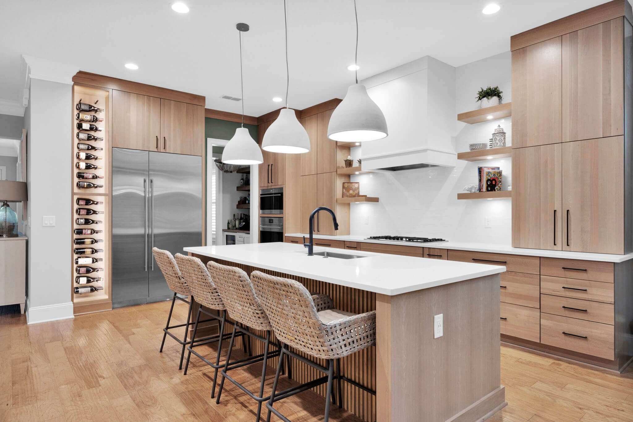 Light stained Quarter-Sawn White Oak kitchen and kitchen island cabinets are contrasted with a beautifully white painted modern wood hood. Modern black cabinet pulls and minimalist detailing create a timeless kitchen design with warmth and contemporary appeal.